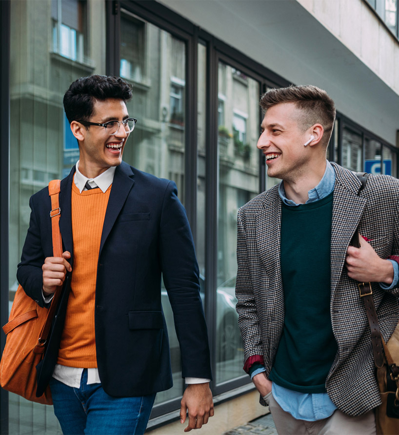 Two people in business attire smiling and laughing while walking down street.