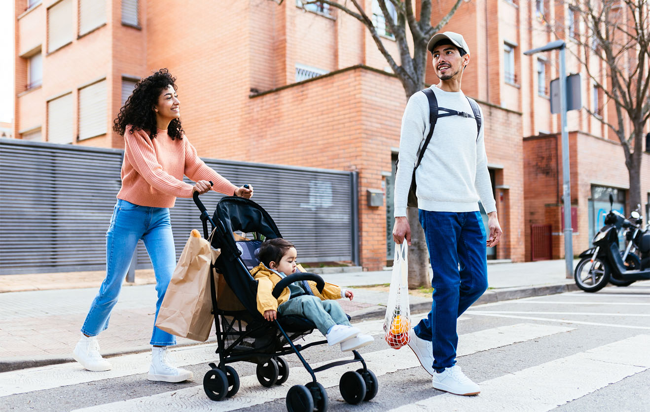 Two parents with baby in stroller walking across street.