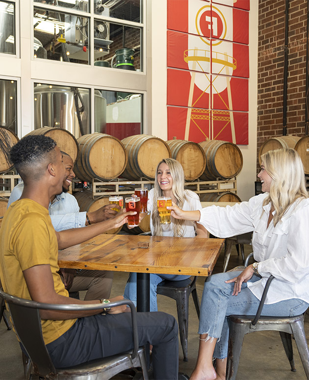 Four friends drinking beer at table in brewery.